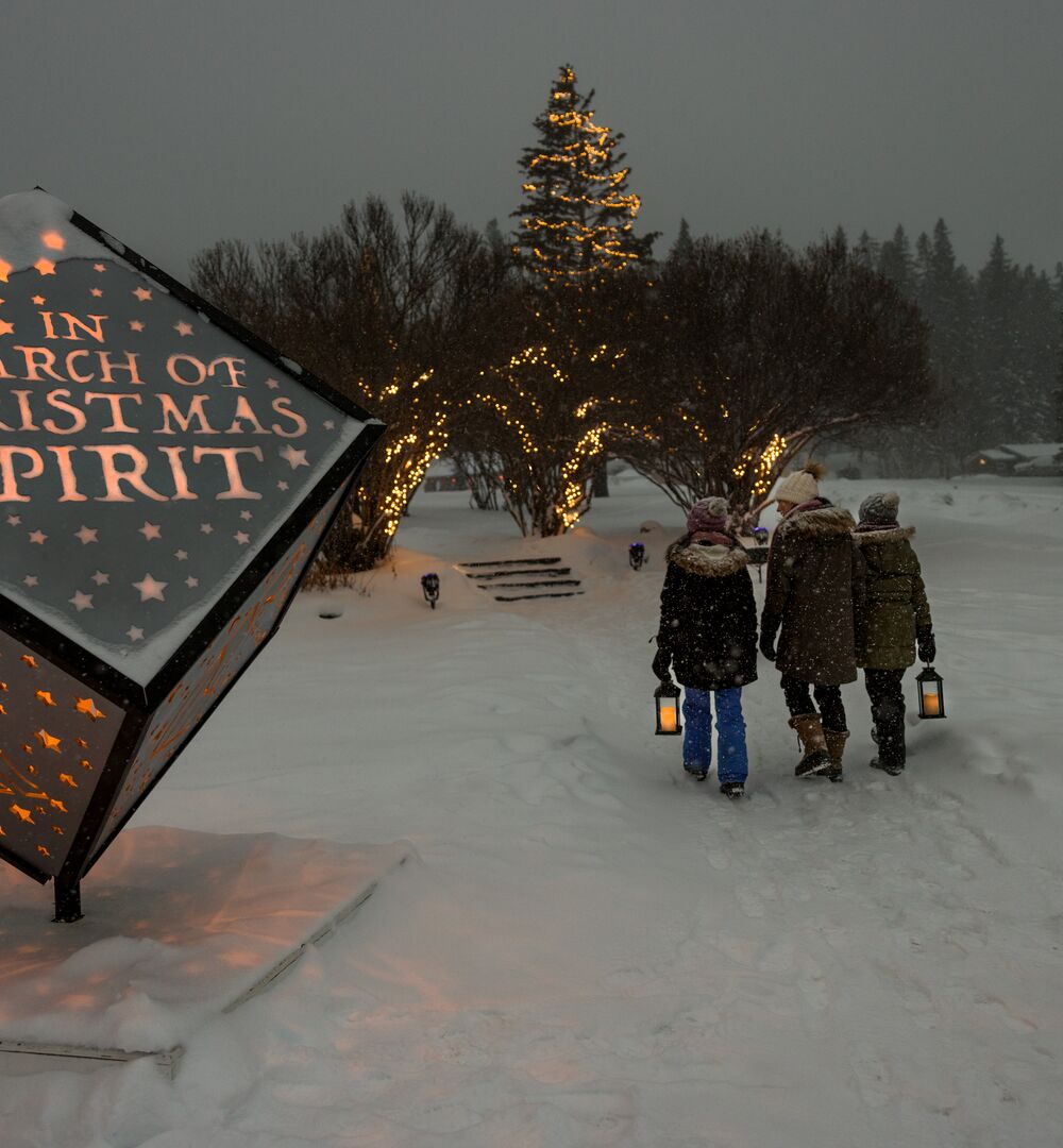 A family enjoys the In Search of Christmas Spirit event featuring light up animal sculptures on a snowy evening in Banff National Park.