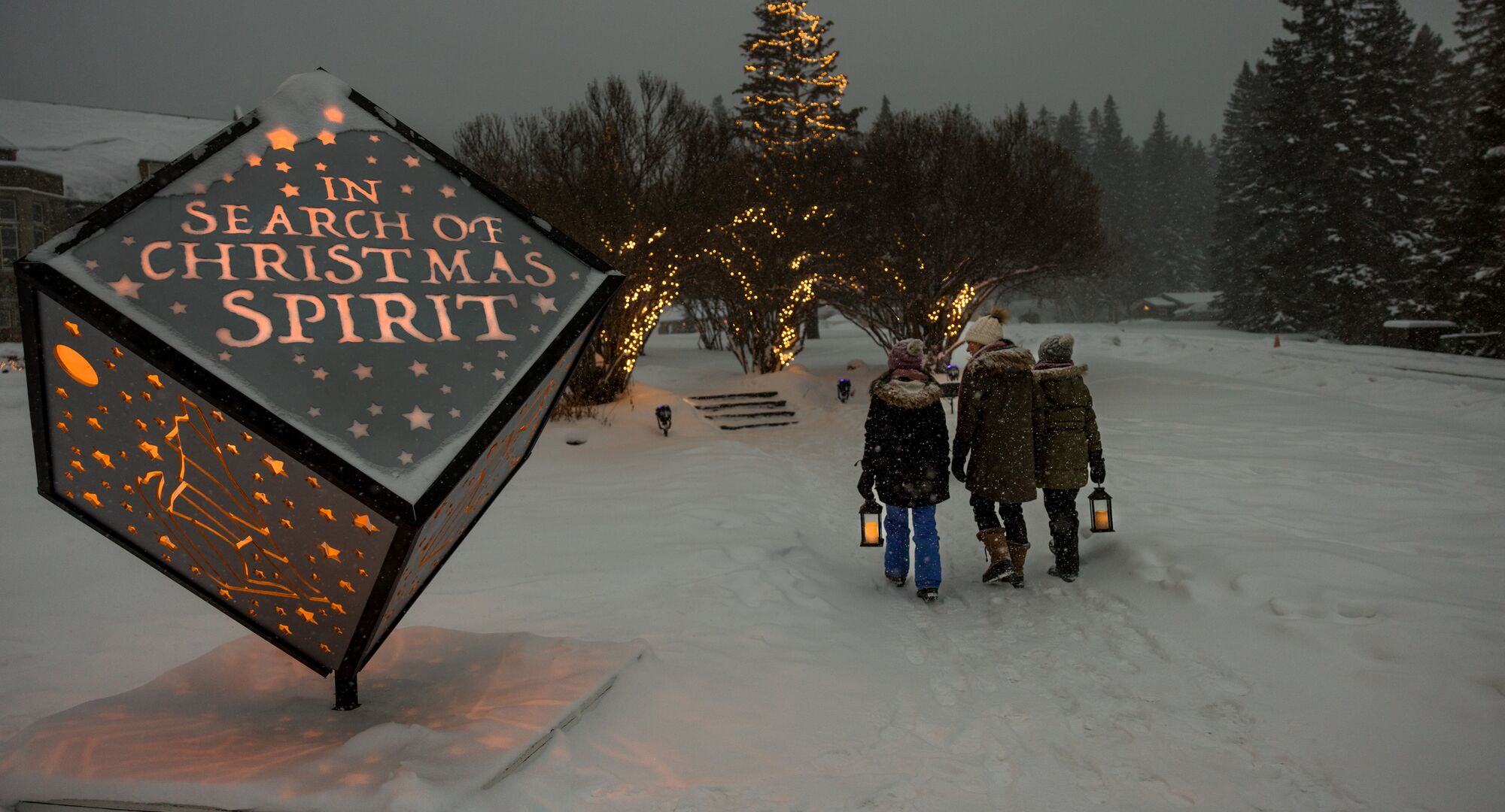 A family enjoys the In Search of Christmas Spirit event featuring light up animal sculptures on a snowy evening in Banff National Park.