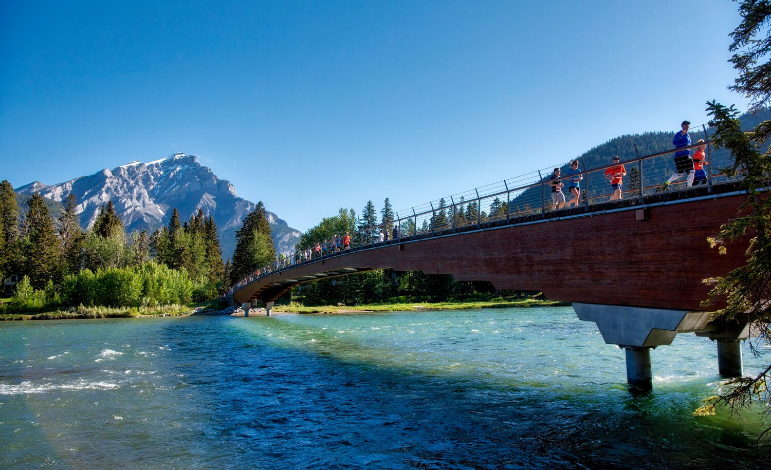 Runners cross the Banff Pedestrian Bridge.
