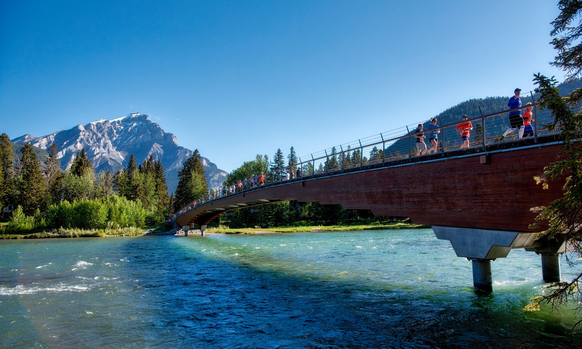Runners cross the Banff Pedestrian Bridge.