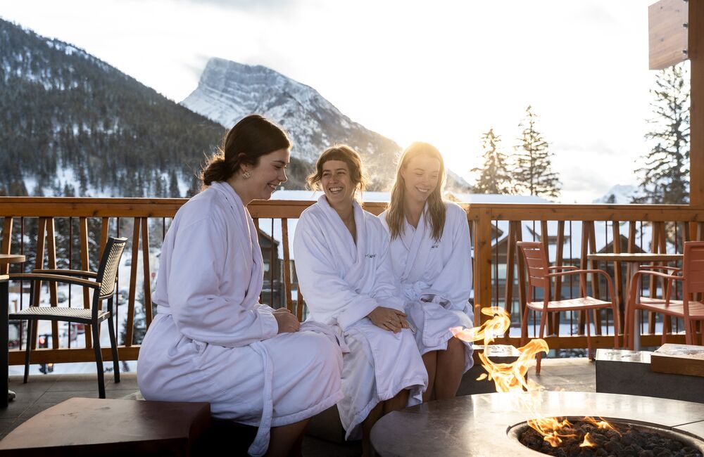 Three friends relax outside around a fire pit at the Meadow Spa at the Moose Hotel in Banff National Park.