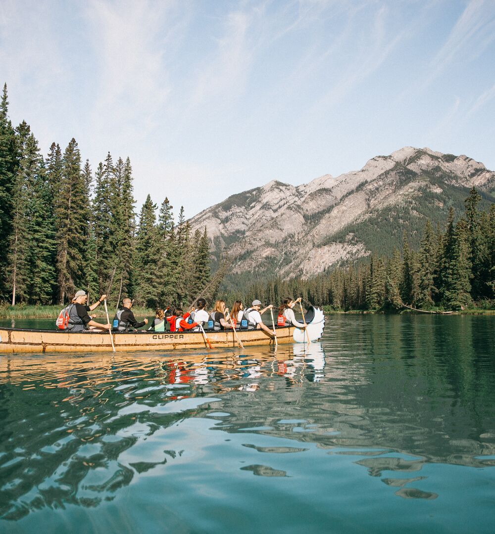 Group of people paddling the Bow River on a Big Canoe Tour with the Banff Canoe Club