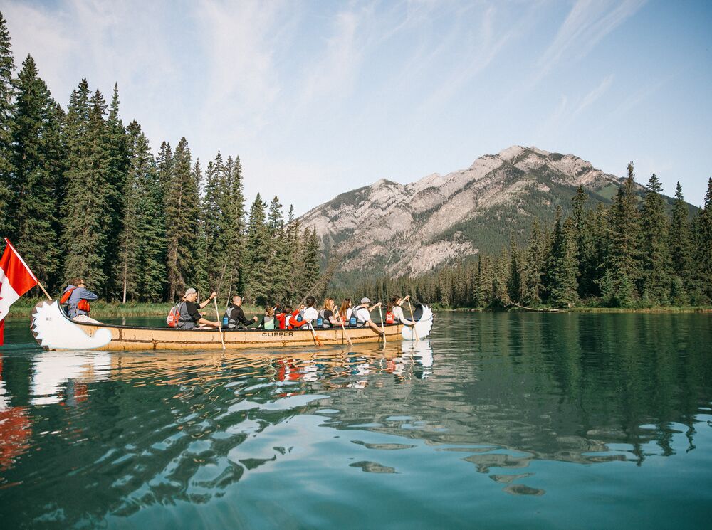 Group of people paddling the Bow River on a Big Canoe Tour with the Banff Canoe Club