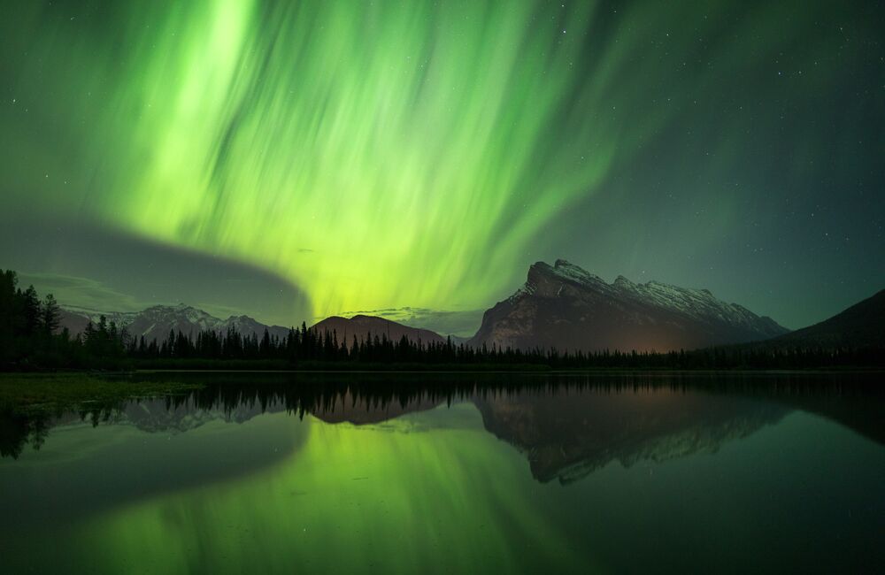 Green aurora glowing over mountains near at Vermilion Lakes in Banff National Park