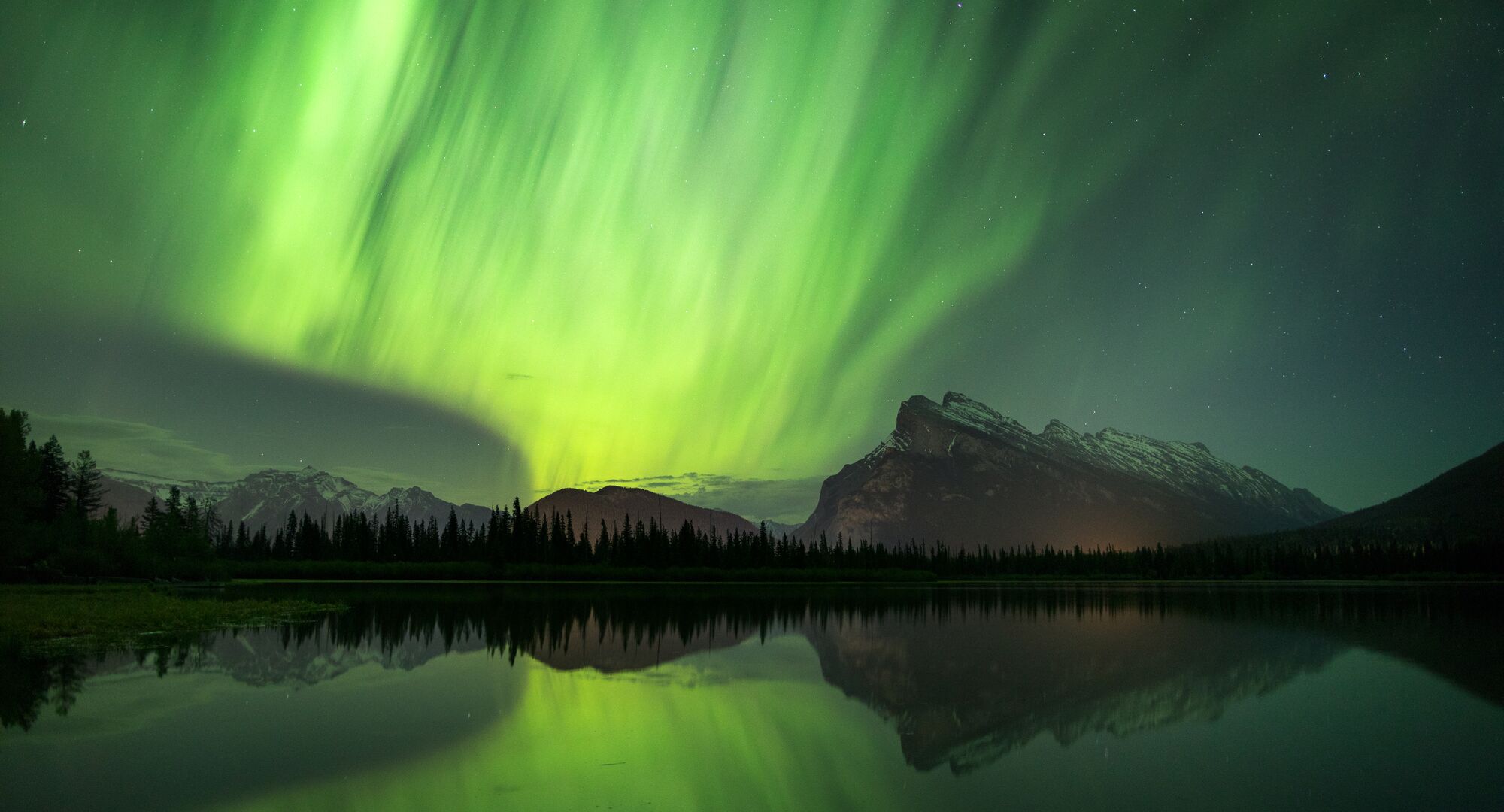 Green aurora glowing over mountains near at Vermilion Lakes in Banff National Park