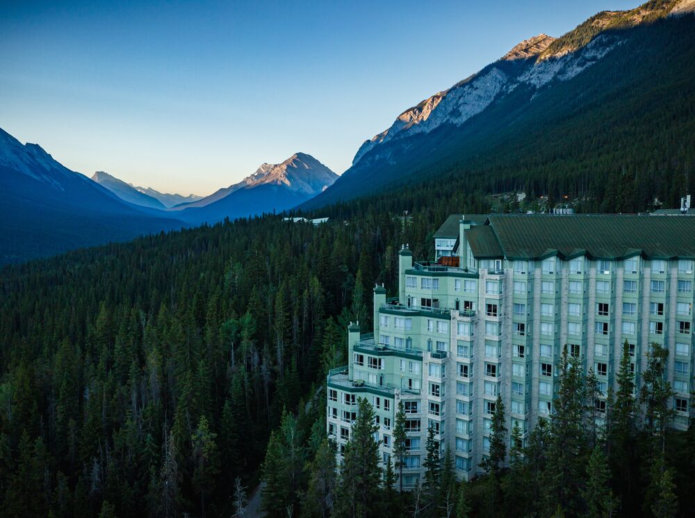 The view of the Rimrock Resort Hotel surrounded by a forest and towering mountains in Banff National Park. 