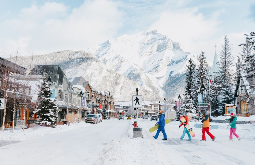 Four snowboarders cross Banff Avenue with Cascade Mountain in the background.