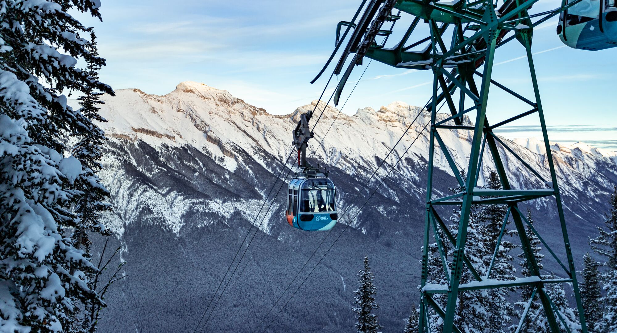 A gondola car travels up towards the top of a snow covered Sulphur Mountain with a clear blue sky above