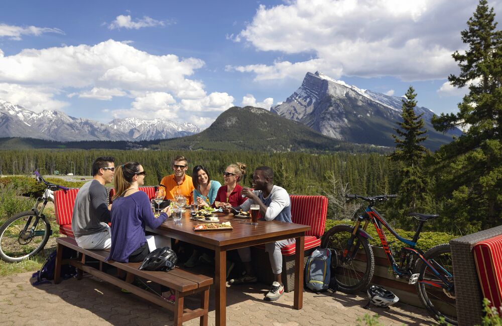 A group of friends enjoy a meal at the Juniper Bistro with a view of Mount Rundle out the window