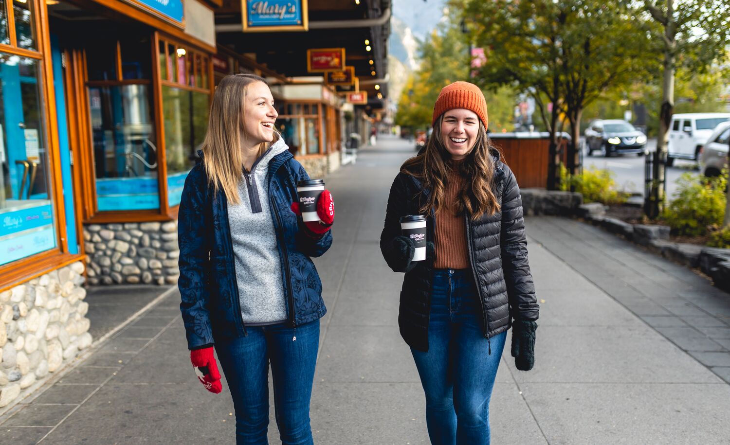 Two people walk down Banff Ave in the fall with coffee cups in hand in Banff National Park.