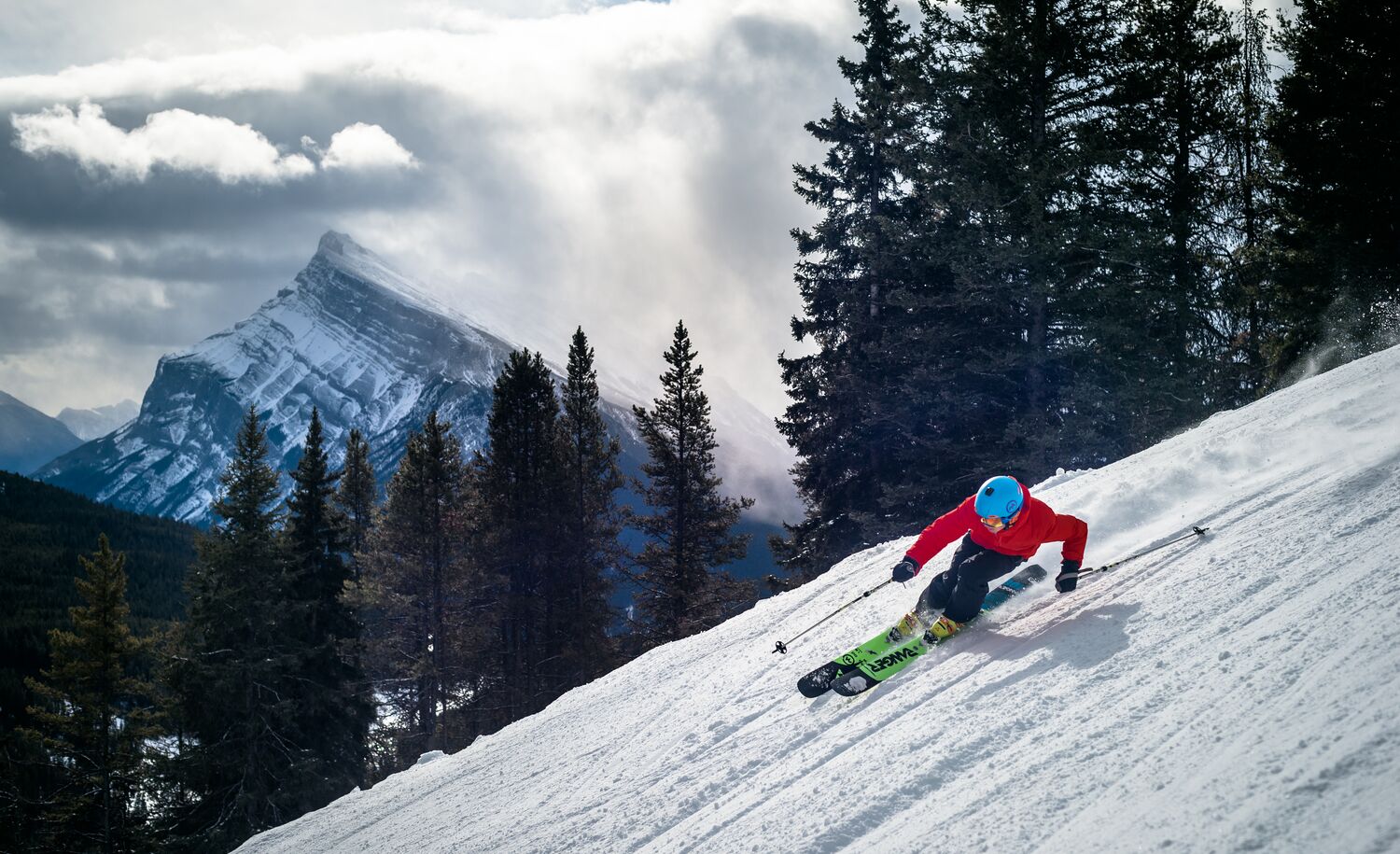 A skier heads down a run at Mt Norquay in Banff National Park with snowy trees and Mount Rundle in the background.