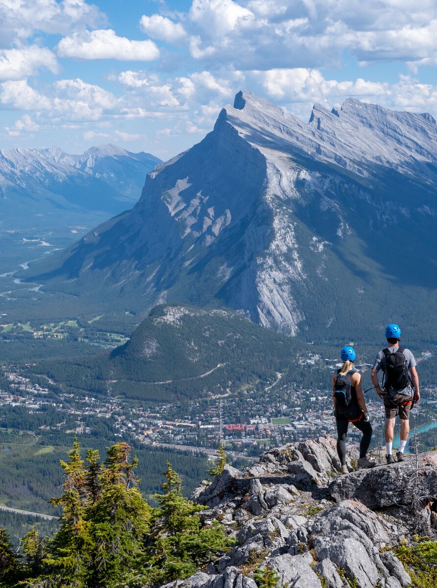 Two people lookout at the Banff townsite from the Mt. Norquay via ferrata on a bluebird day with views of Mount Rundle.