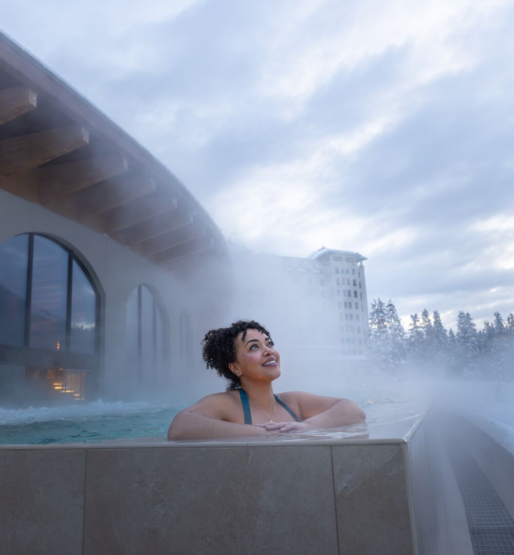 A woman in an outdoor hot tub gazing up at the sky at BASIN Glacier Waters in Lake Louise
