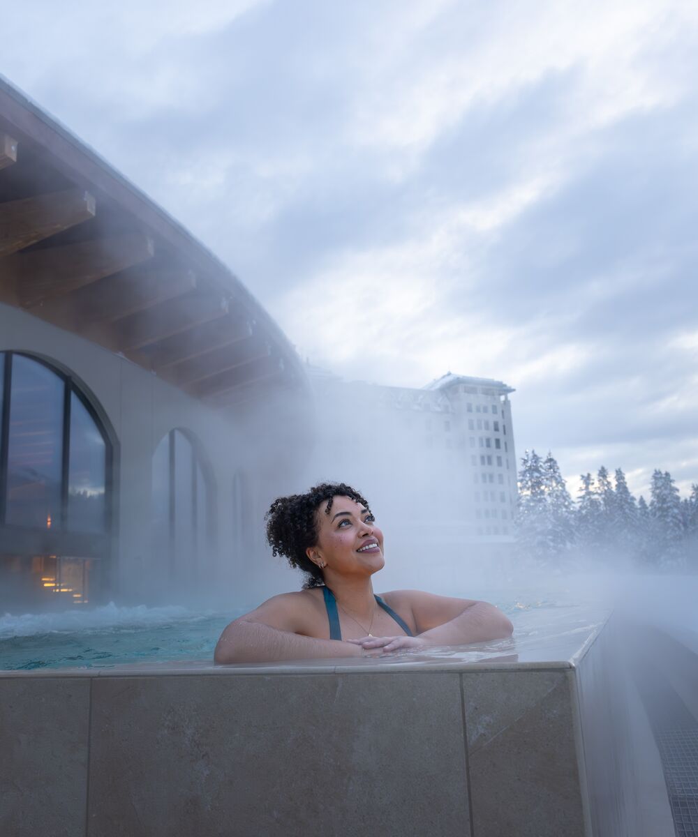 A woman in an outdoor hot tub gazing up at the sky at BASIN Glacier Waters in Lake Louise