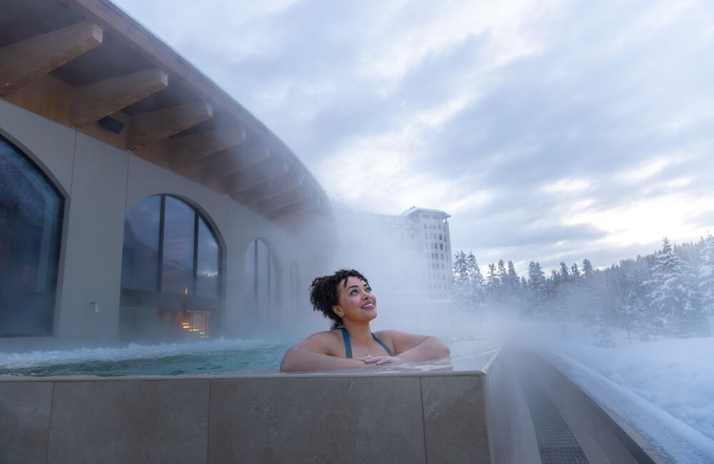 A woman in an outdoor hot tub gazing up at the sky at BASIN Glacier Waters in Lake Louise