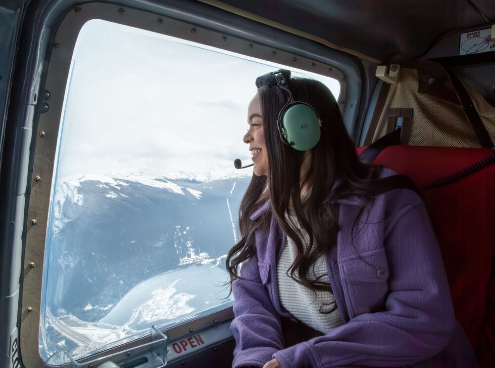 A woman looks out the window of a helicopter towards a mountain range and lake during a tour near Banff National Park.