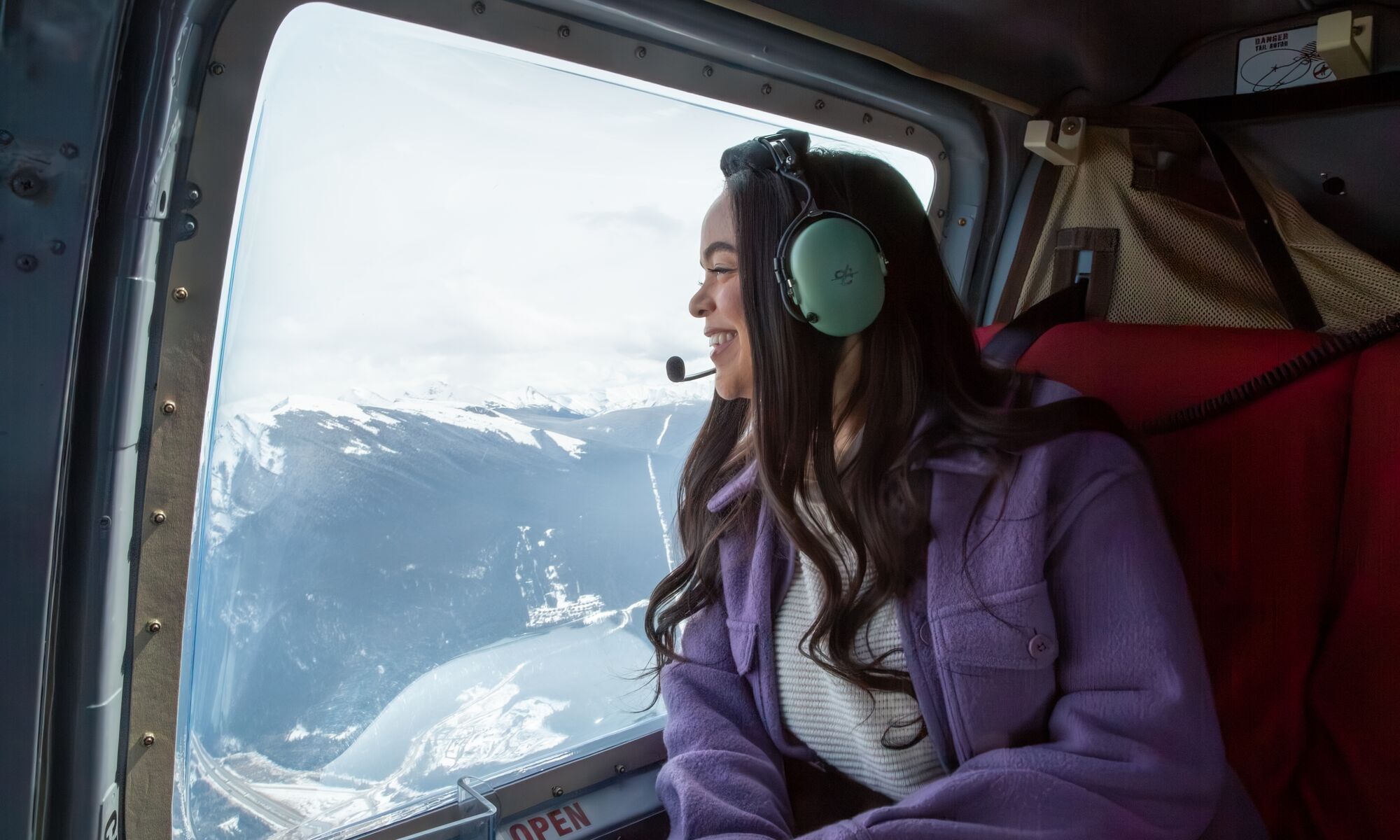 A woman looks out the window of a helicopter towards a mountain range and lake during a tour near Banff National Park.