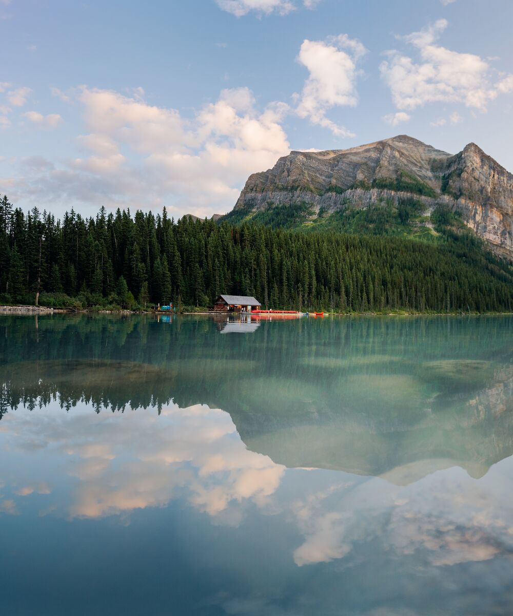 A view of turquoise Lake Louise from the shoreline on a summer day at sunset.