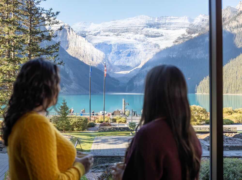 Two people look at the view of Lake Louise from the window of a restaurant that supports dietary restrictions at the Chateau Lake Louise in Banff National Park.