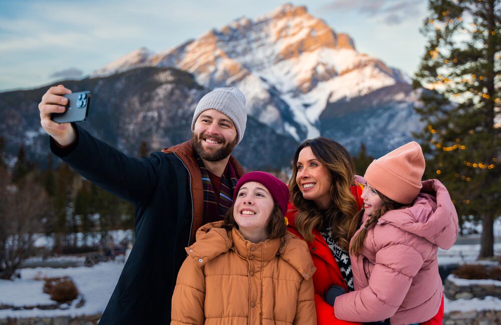 A family takes a selfie at Cascade of Time Gardens with Cascade Mountain in the background in the Banff townsite.