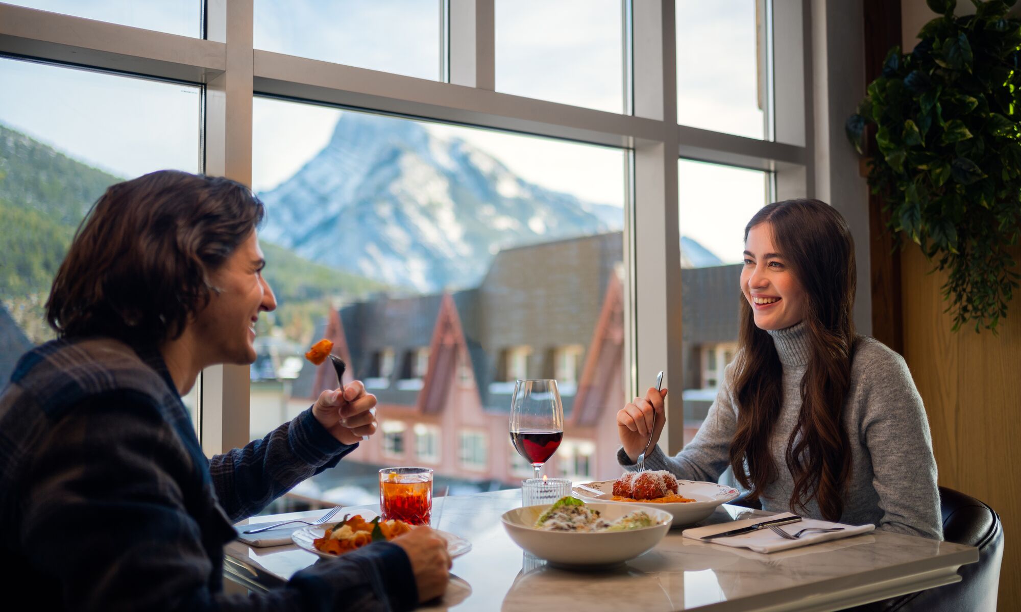 A couple dines at Lupo in Banff National Park with Mount Rundle out the window in the background.